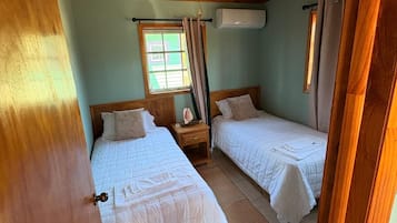 Une chambre avec deux lits, un plafond en bois, une fenêtre avec des rideaux et un appareil de climatisation.