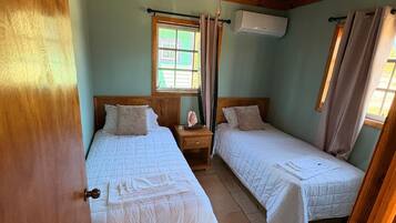 Une chambre avec deux lits, un plafond en bois, un appareil de climatisation et une fenêtre avec des rideaux.