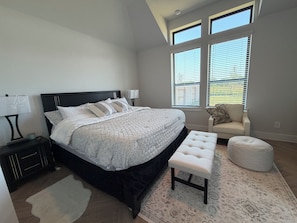 A bedroom with a large bed, bedside tables, a bench, and a window with blinds. - Modern 4 bedroom retreat spacious family friendly. (Katy)