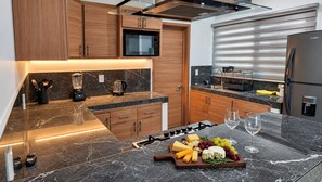 Eine moderne Küche mit Holzschränken, einer eingebauten Mikrowelle, einem Edelstahlkühlschrank und einer Marmorarbeitsplatte.