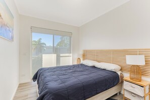 Ein Schlafzimmer mit Bett, Nachttisch, Lampe und Blick durch ein Fenster.