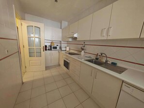 A kitchen with white cabinets, a microwave, a stove, and a sink. - Apartment Sleeps 8 with Pool and Parking (Malaga)