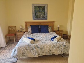 A hotel room with a bed, two bedside tables, a chair, a painting on the wall, and a carpeted floor. - Apartment Sleeps 8 with Pool and Parking (Malaga)