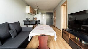 A modern living space with a sofa, a dining table, a TV, and a kitchen area. - Gdańsk Koprowskiego Apartment #18 (Gdańsk)