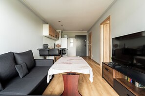 Un espacio habitable moderno con sofá, mesa de comedor, televisor y zona de cocina.