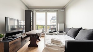 A modern bedroom with a TV, a bed with pillows, a bedside table, and a view of the outside. - Gdańsk Koprowskiego Apartment #18 (Gdańsk)