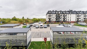 A parking lot with multiple cars, a building with balconies, and a green area with trees. - Gdańsk Koprowskiego Apartment #18 (Gdańsk)