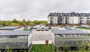 Un estacionamiento con varios coches, un edificio con balcones y una zona verde con árboles.
