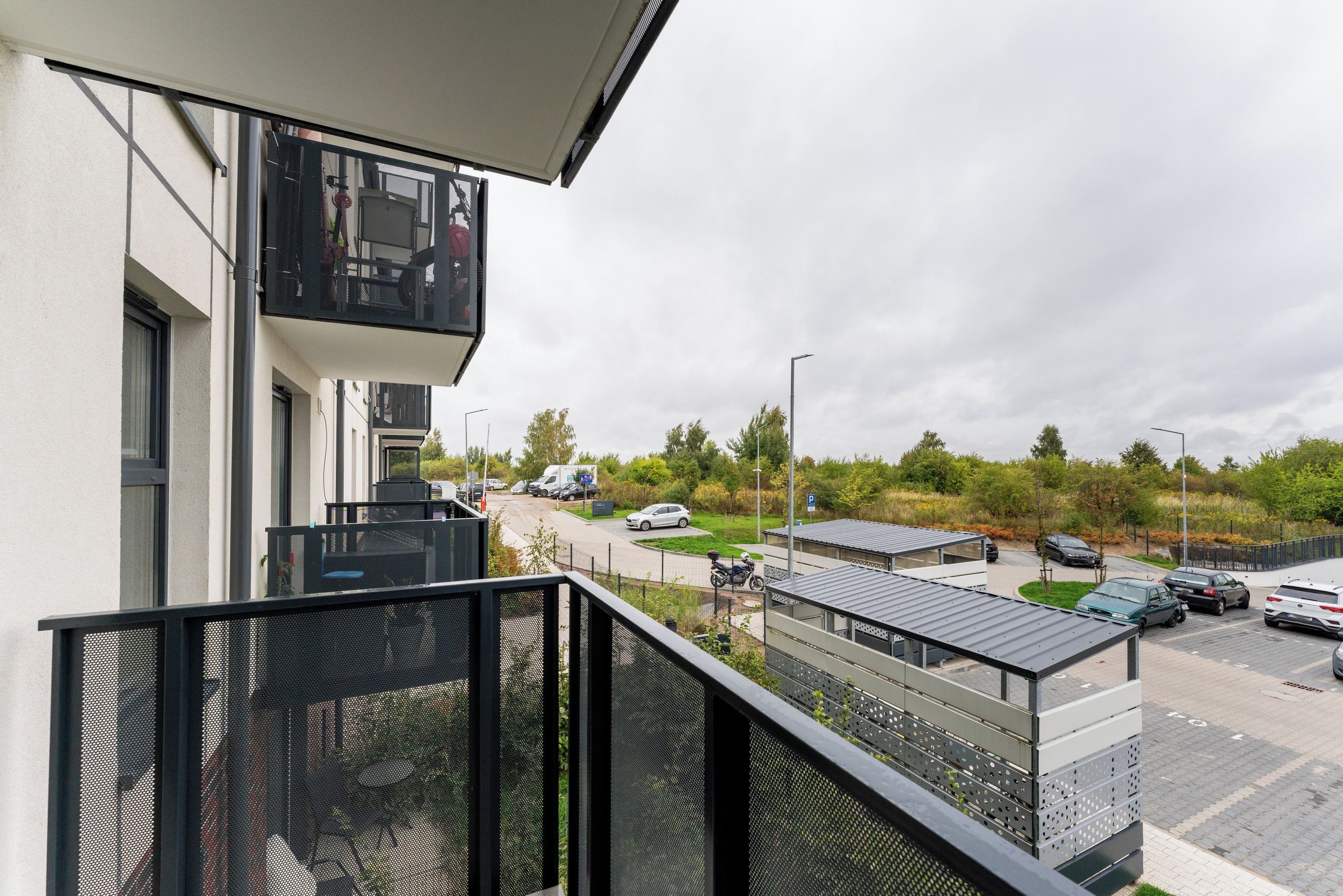 Un edificio moderno con balcón, vista a un estacionamiento y una carretera con vehículos.