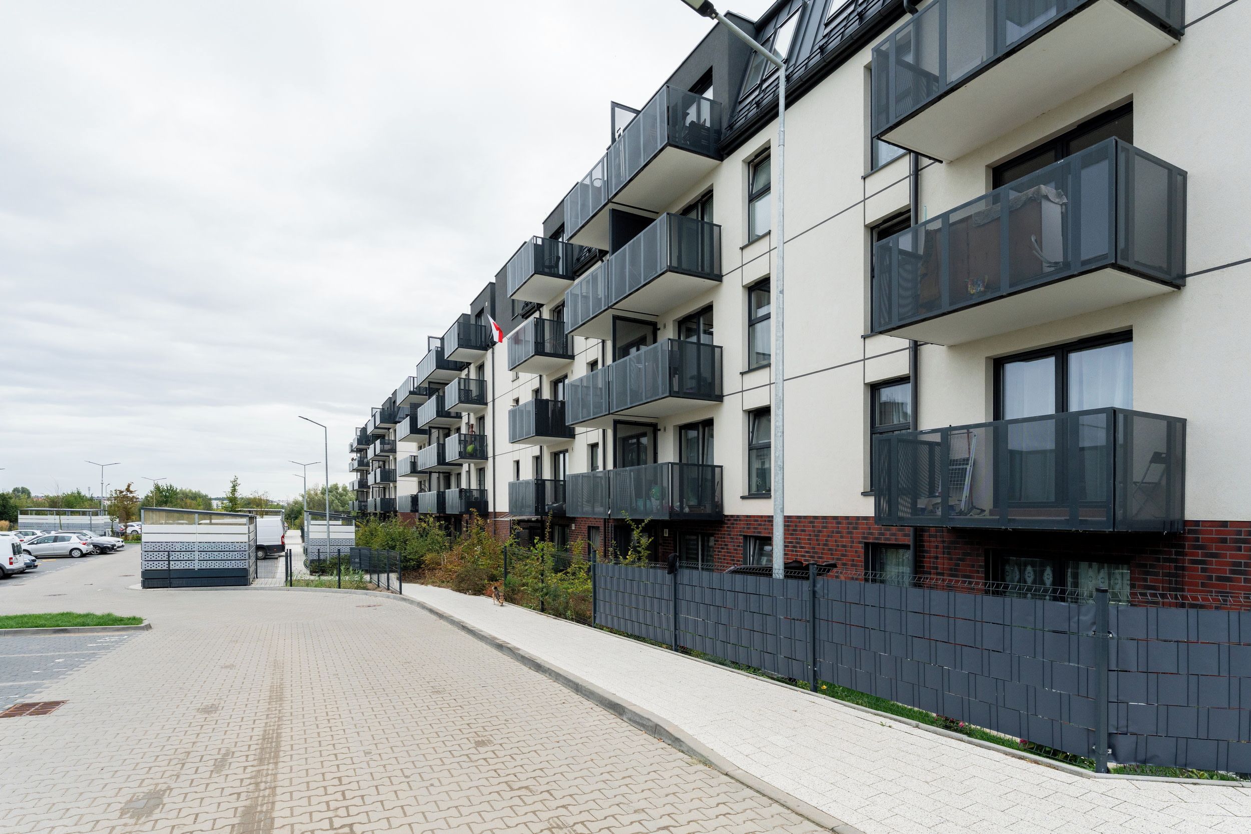 A modern multi-story residential building with balconies and a paved driveway.