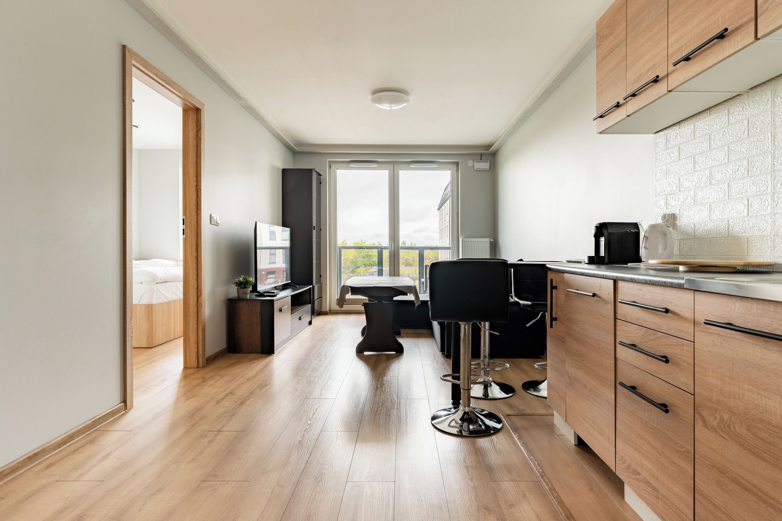 A modern kitchen with wooden cabinets, a dining area with a table and chairs, and a large window providing a view of the outside.