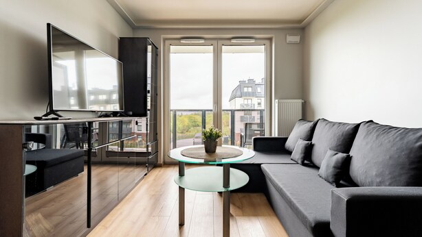 Een moderne woonkamer met een glazen salontafel, een grijze bank en een flatscreen televisie.