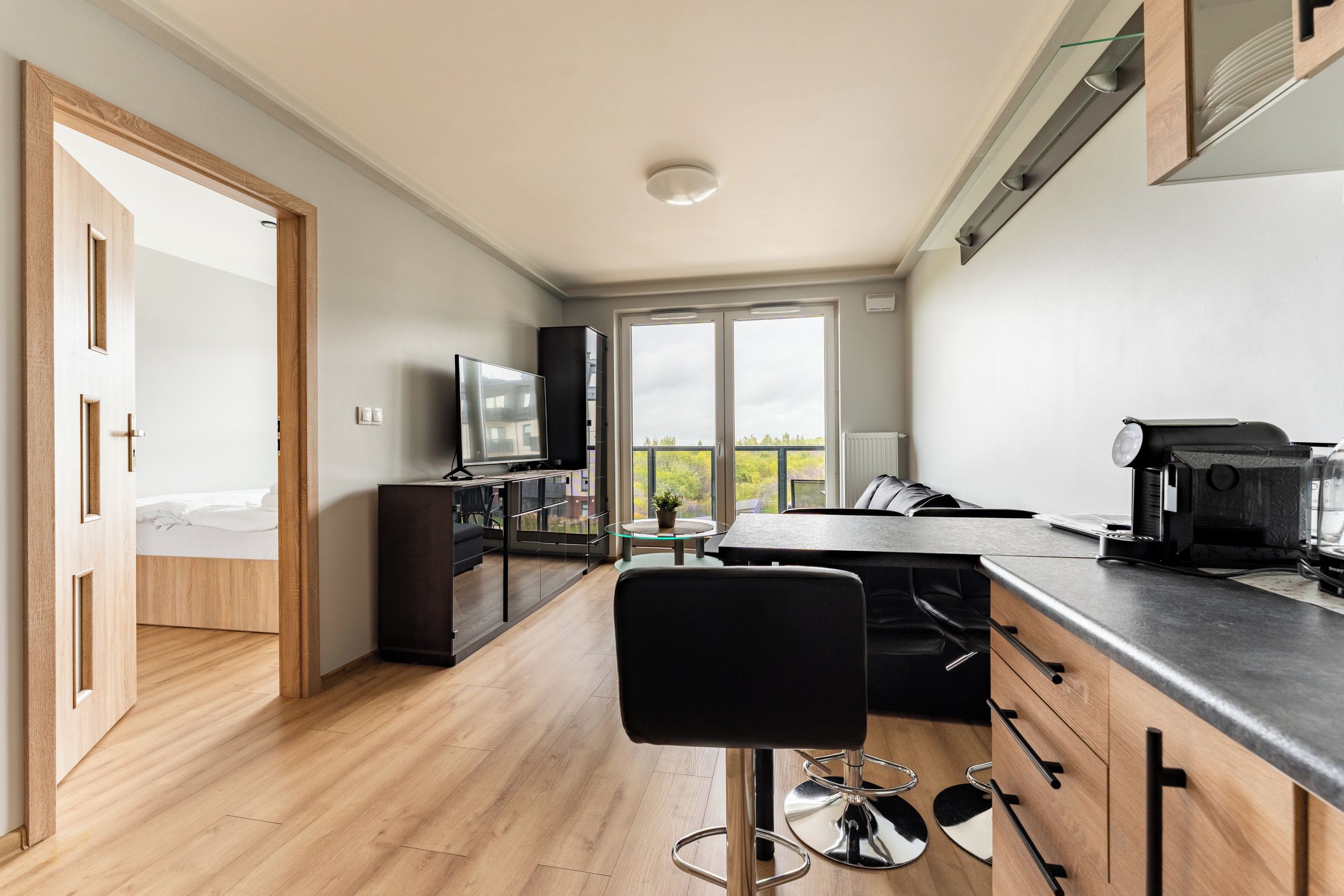 A modern kitchen with a dining area, a bar stool, and a television.