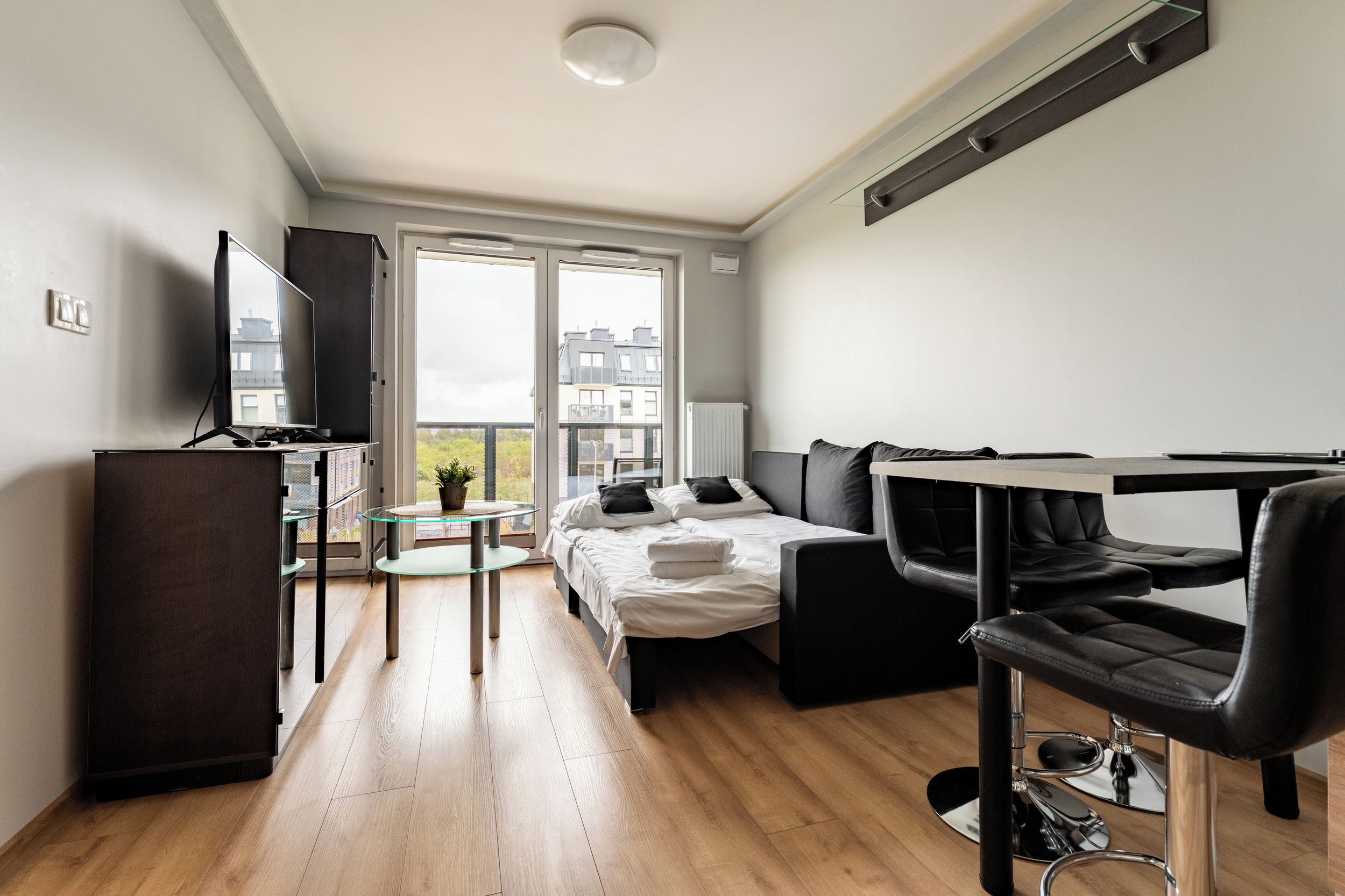 A modern, well-lit room with a bed, a sofa, a desk, and a TV.
