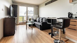 Een moderne woonkamer met een bank, een salontafel, een televisie en een keukenhoek met een koffiezetapparaat.
