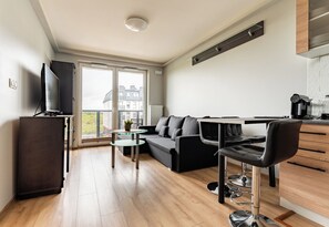 A modern living room with a sofa, a coffee table, a TV, and a kitchen area with a coffee machine. - Gdańsk Koprowskiego Apartment #34 (Gdańsk)