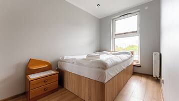 Une chambre à coucher avec un lit en bois, une table de chevet en bois dotée de tiroirs, une fenêtre avec vue et un radiateur.