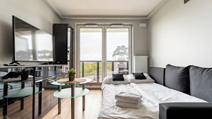 Een moderne slaapkamer met een bed, een televisie, een glazen tafel en een balkon met uitzicht op de stad.