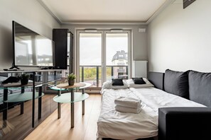 A modern bedroom with a bed, a TV, a glass table, and a balcony with a city view. - Gdańsk Koprowskiego Apartment #34 (Gdańsk)