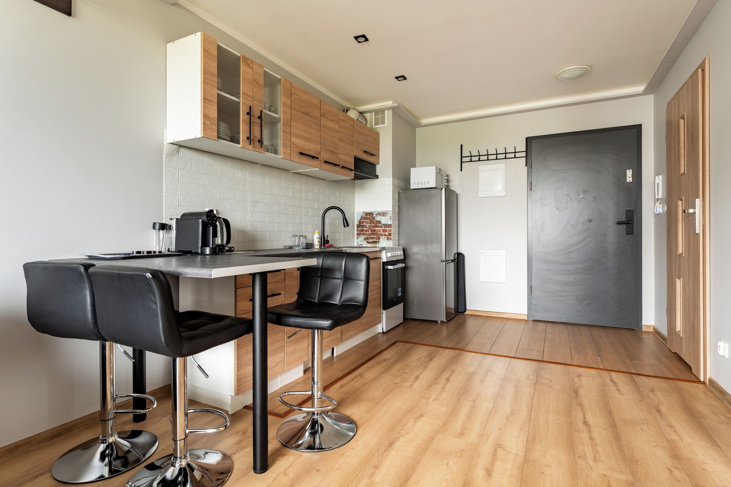 A modern kitchen with a bar area, stainless steel appliances, and a wooden floor.