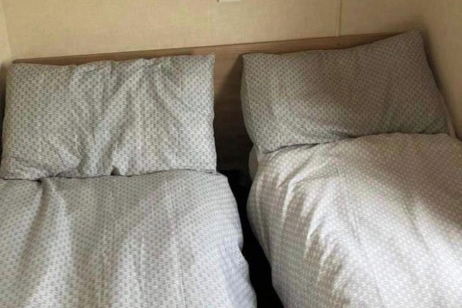 Huoneessa on kaksi sänkyä, joissa kummassakin on kuviollinen päiväpeite ja tyynyjä.