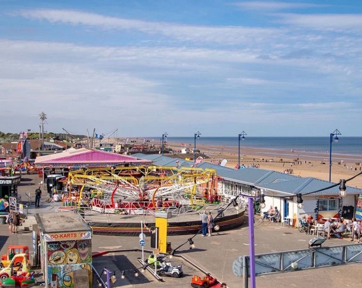 A coastal amusement park with rides and beachside seating.