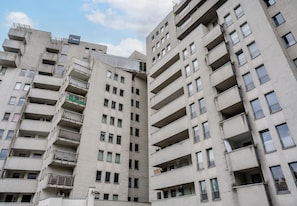 Um edifício residencial com vários andares, varandas, uma placa de identificação de comércio e um céu claro.