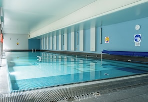 Uma piscina interior com pistas demarcadas, sinais de segurança e um relógio na parede.