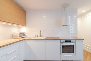 Eine moderne Küche mit weißen Schränken, einer Holz Arbeitsplatte, einer eingebauten Mikrowelle, einem Waschbecken mit Goldarmatur und einem Einbauofen.
