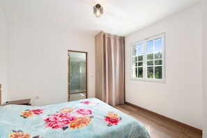Ein Schlafzimmer mit Bett, Fenster, Tür und einer Duschkabine.