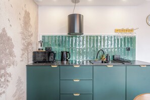 A kitchen with a green countertop, a black range hood, and a stainless steel sink. - Dyrekcyjna Signature Studio (Katowice)