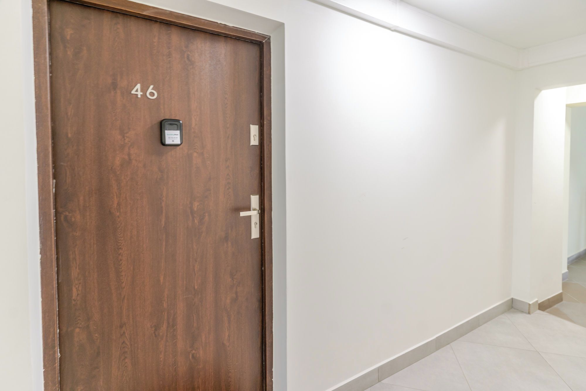 A hallway with a wooden door marked with the number 46, a keycard reader, and a light switch.