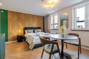 A hotel room with a bed, bedside table, chairs, a round dining table, a mirror, and a window. - Dyrekcyjna Signature Studio (Katowice)