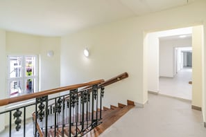 A staircase with a wooden handrail and metal balusters, leading to a hallway with a white tiled floor and a door with a view of a balcony. - Dyrekcyjna Signature Studio (Katowice)