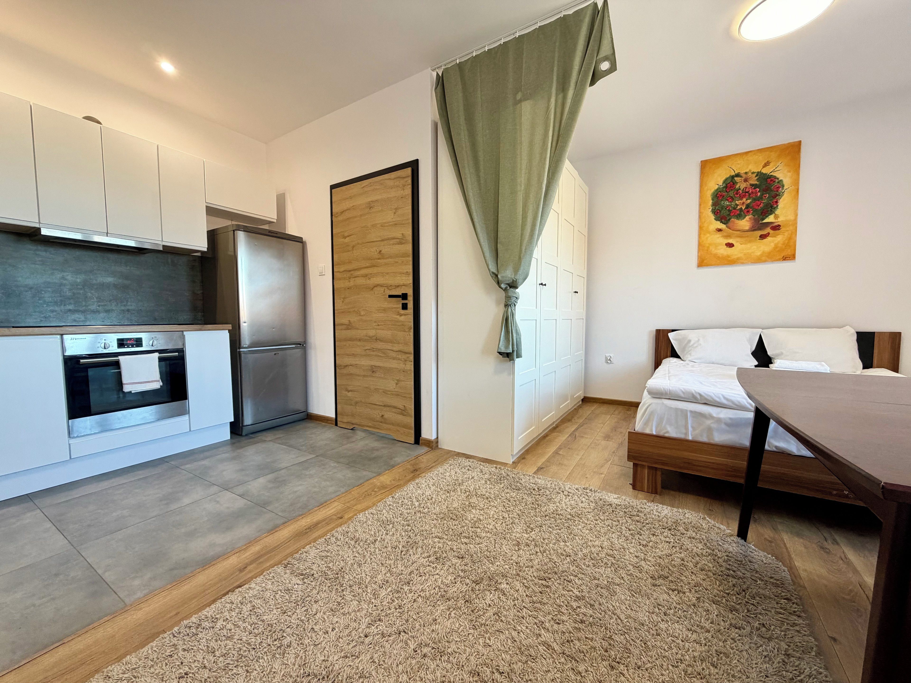 Eine moderne Küche mit Einbauofen und Kühlschrank, einer Holztür sowie einem Essbereich mit Tisch und Stühlen.