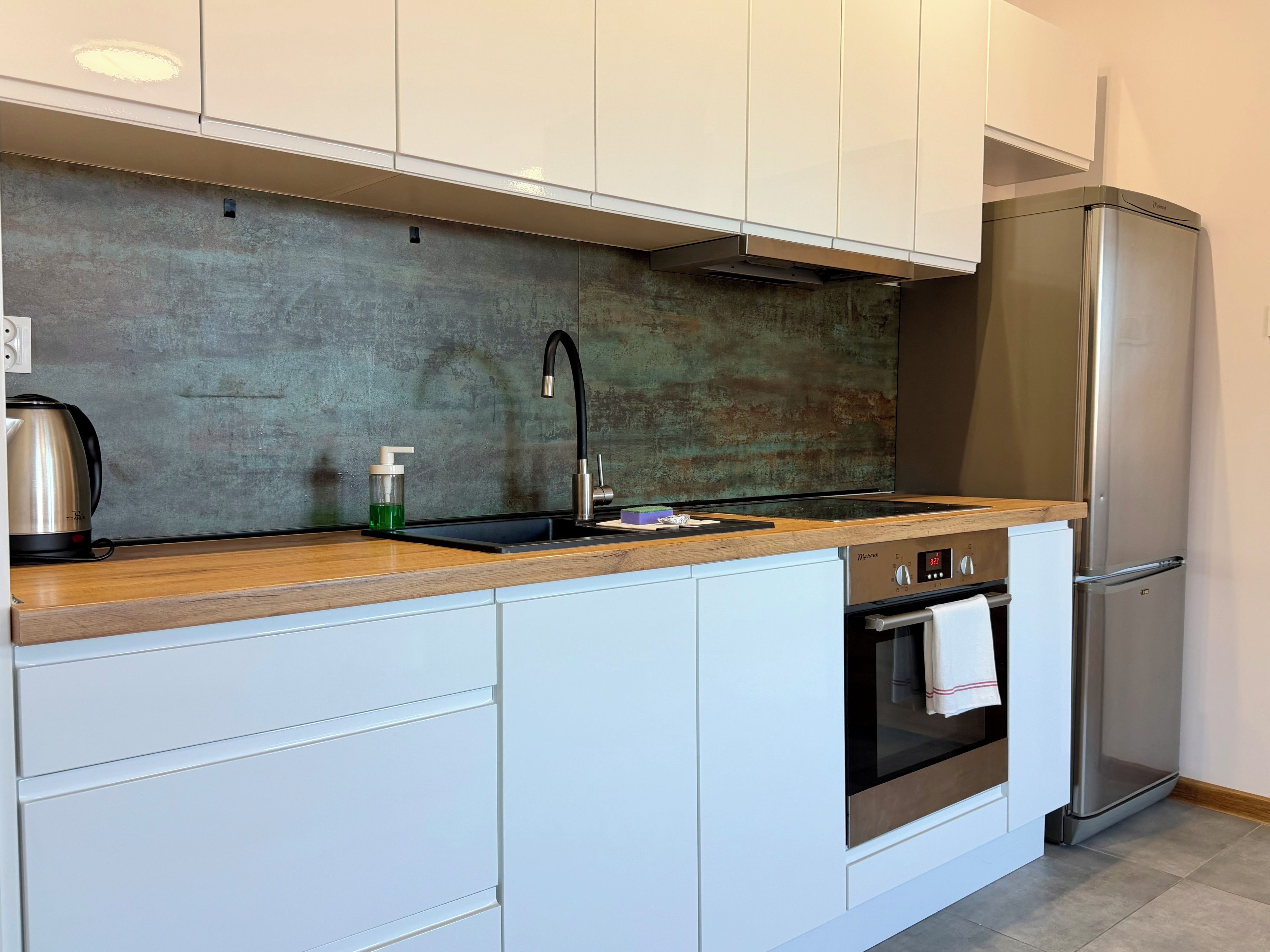 Eine moderne Küche mit weißen Schränken, einem Edelstahl-Kühlschrank, einem eingebauten Ofen und einer Holz Arbeitsplatte.