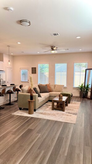 A modern living room with a sectional sofa, a coffee table, and a dining area with bar stools. - Modern Cozy Retreat Minutes From Downtown Houston (Houston)
