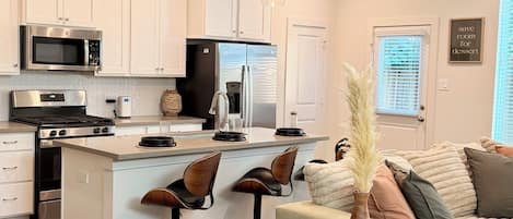 A modern kitchen with white cabinetry, a central island, and bar stools.