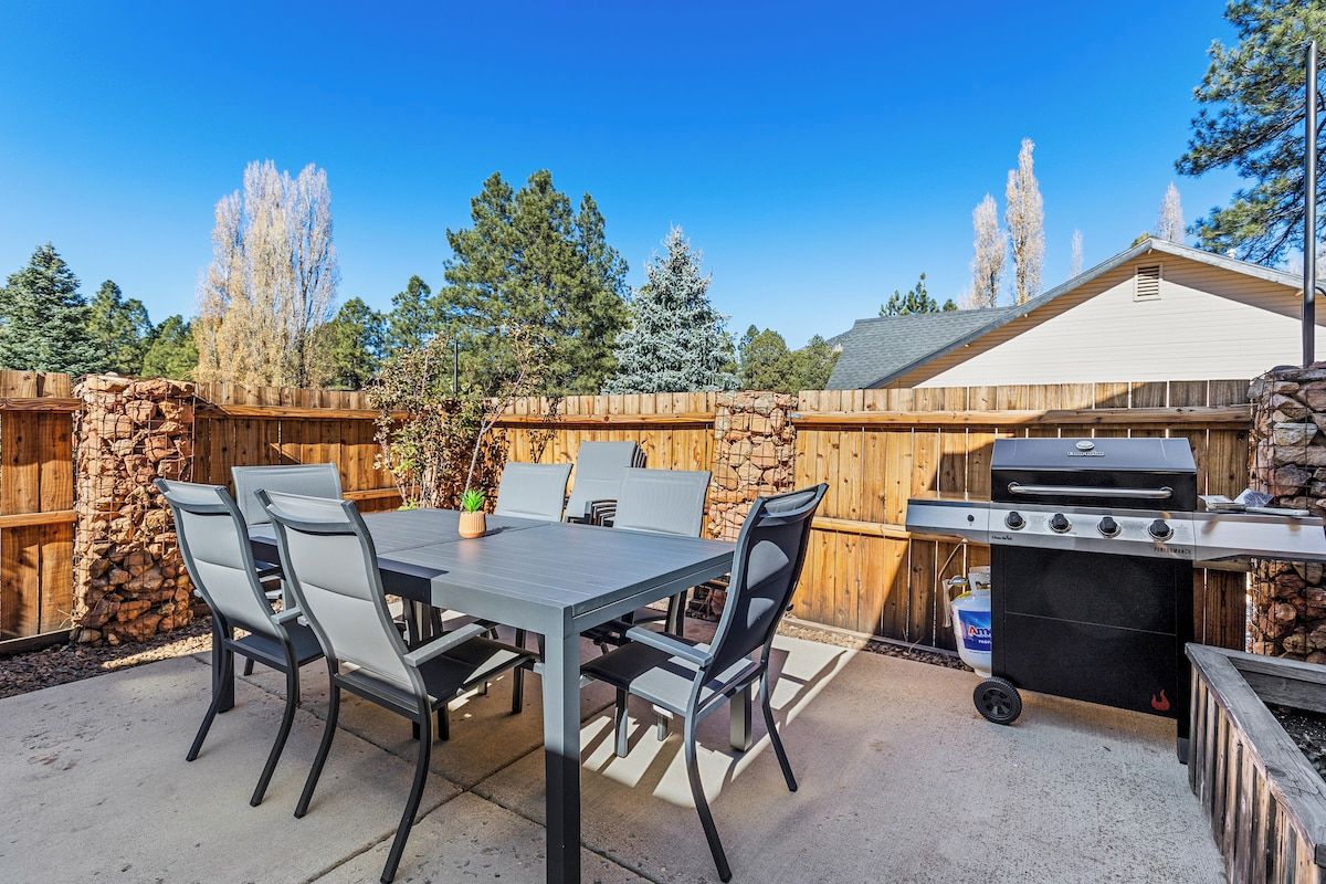 Een terras buiten met een tafel, stoelen, een barbecue en een stenen muur.