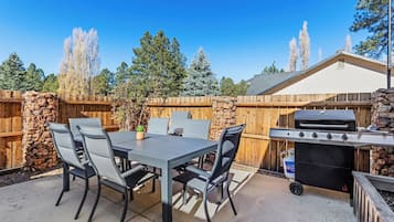 Een terras buiten met een tafel, stoelen, een barbecue en een stenen muur.