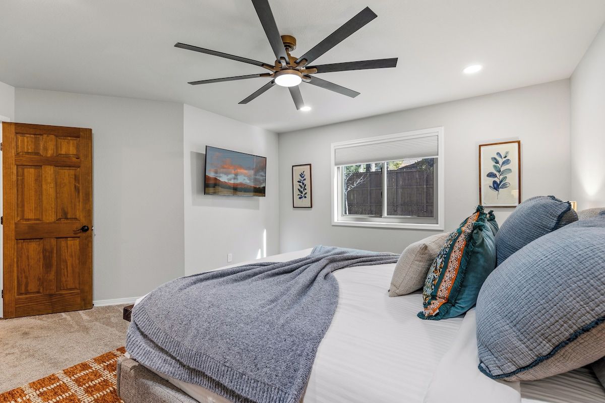 A bedroom with a bed, a ceiling fan, a window, and a door.