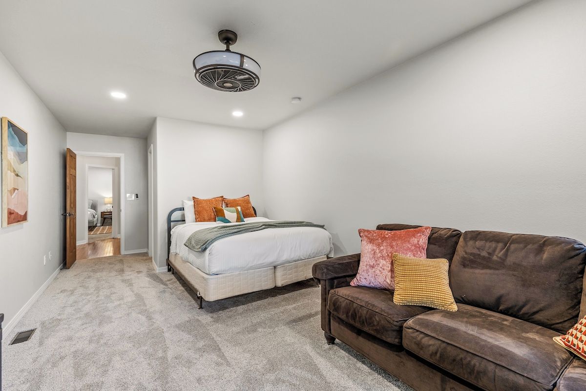 A bedroom with a bed, a brown leather couch, and a ceiling fan.