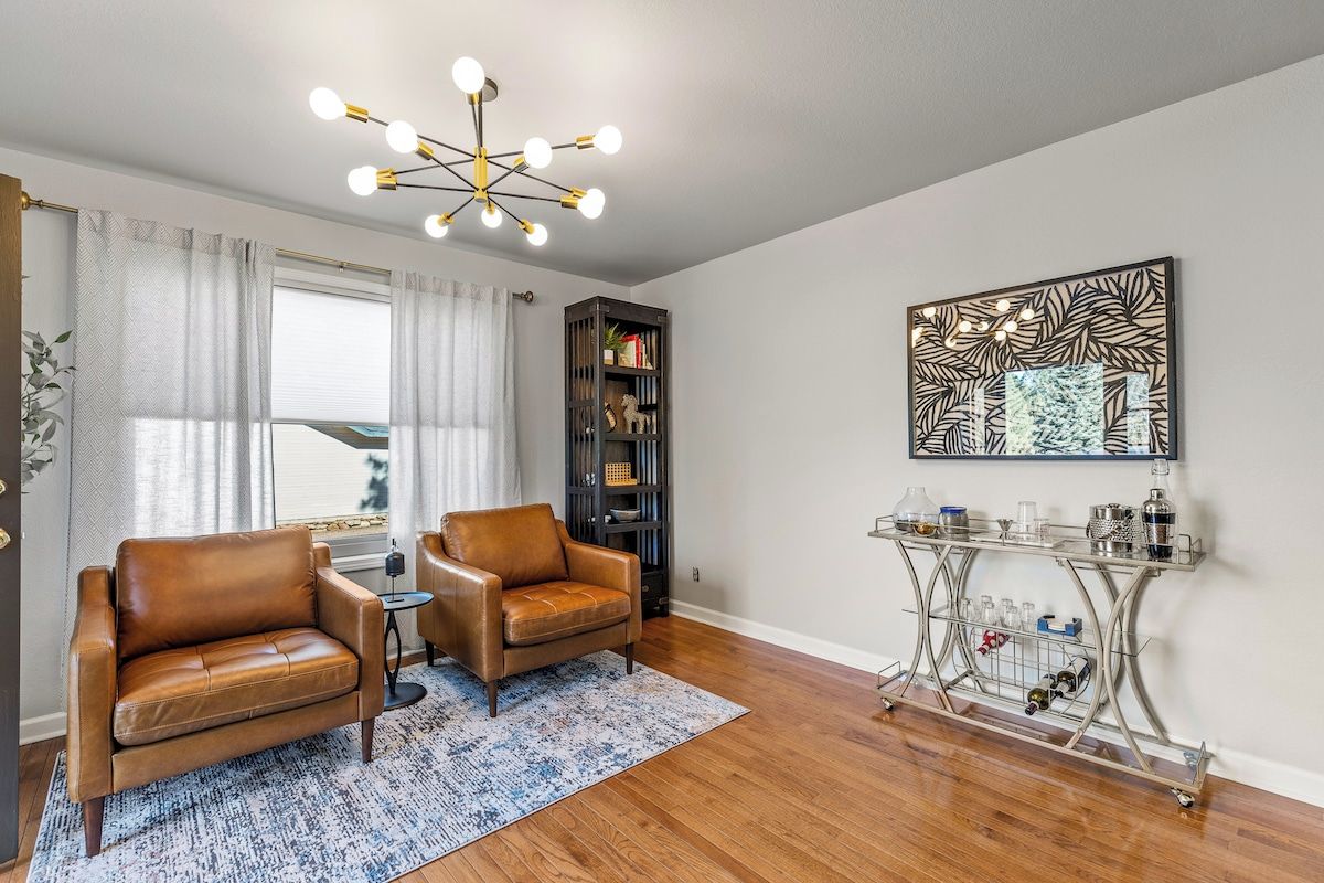 A living room with two leather sofas, a coffee table, a bookshelf, a decorative wall piece, and a metal console table with bottles.