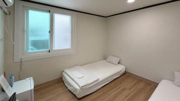 A small, single-bed room with a wooden floor, a window with frosted glass, and a white wall.
