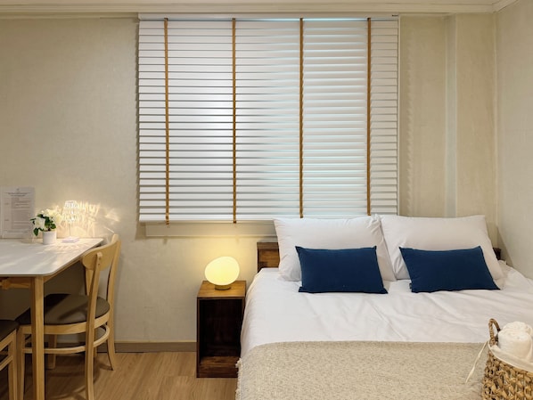 Un dormitorio con cama, mesita de noche, lámpara y ventana con persianas.