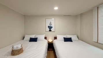 Habitación de hotel con dos camas, una mesita de noche con lámpara, una obra de arte en la pared y una ventana con persianas.