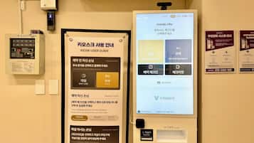 Habitación de hotel con un quiosco digital para servicios a huéspedes, un panel de control con varios botones y un detector de incendios instalado.
