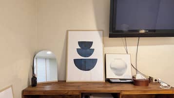 Una habitación con un escritorio de madera, un televisor de pantalla plana, un cuadro abstracto enmarcado, un jarrón y un refrigerador pequeño.