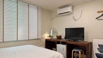 Habitación de hotel con dos camas, un escritorio con televisor, un refrigerador pequeño y aire acondicionado.
