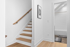 A staircase with wooden steps and a handrail, leading to a room with white walls and a framed picture. - Juniper & Jukebox - Movie Room, Rooftop w/ Mural & Fire Pit, 5 Bedrooms, 9 bed (Nashville)